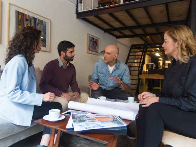 Interior designer presenting renovation project Interior designer presenting renovation project and discussing blueprint with clients. Group of people sitting on couch at home and talking. Renovation project concept